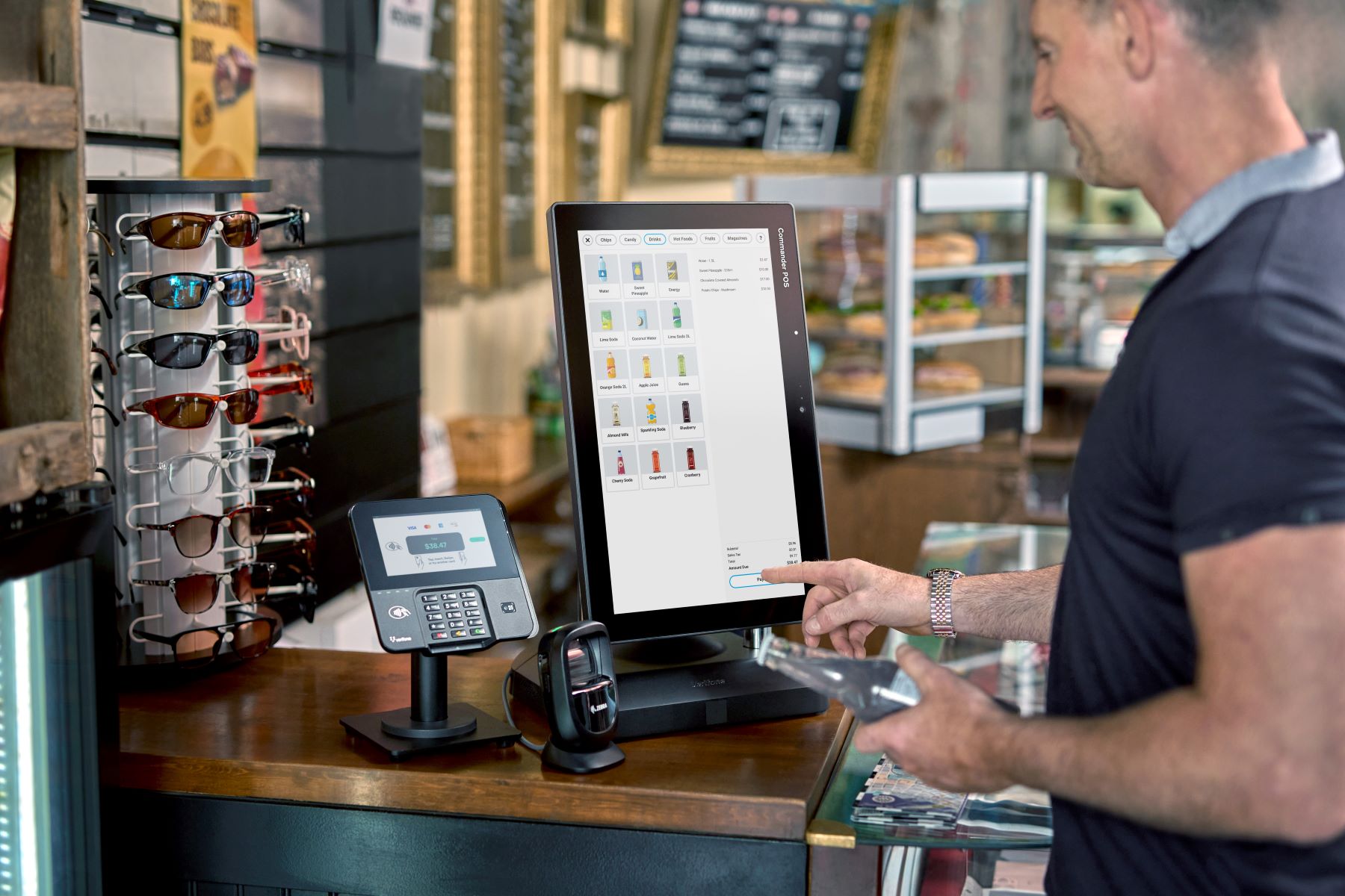 Man using touchscreen point-of-sale system to pay for a bottle in a cafe with pastries in the background.